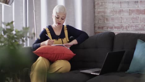 mujer biracial ocupada trabajando en casa con computadora portátil en el sofá en cámara lenta