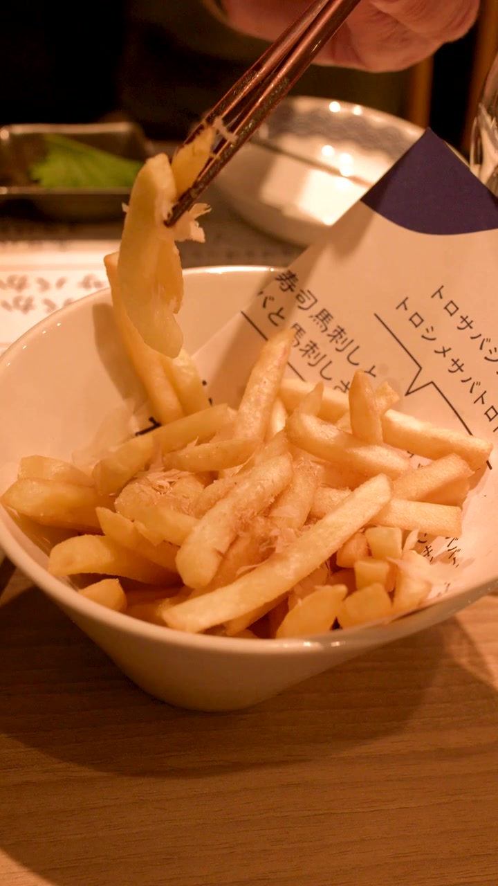 Close-up of hands using wooden chopsticks to lift a french fry from a bowl