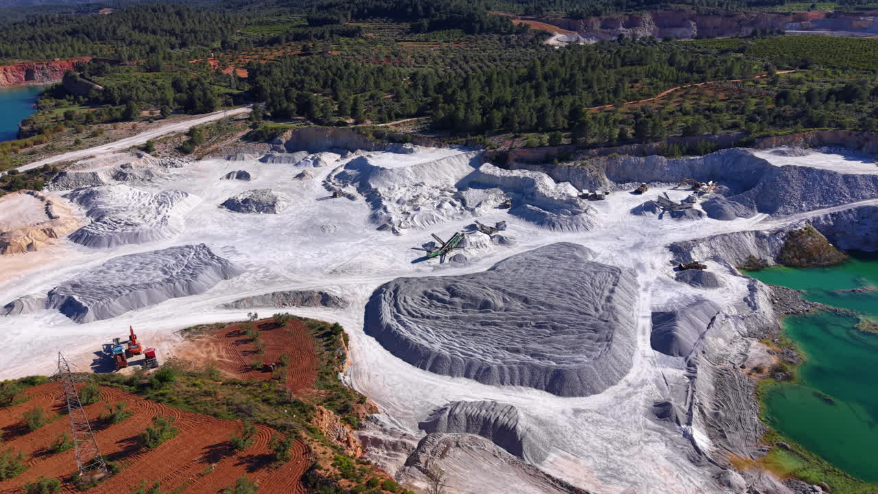 Suuri avolouhos kipsikaivos, jossa on valkoisia mineraaliesiintymiä, raskasta kalustoa, turkooseja vesialtaita ja ympäröivä vihreä metsämaisema.