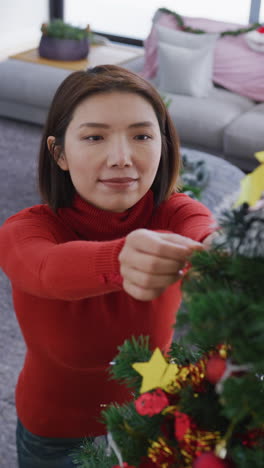 video vertical de una mujer asiática feliz decorando el árbol de navidad en casa