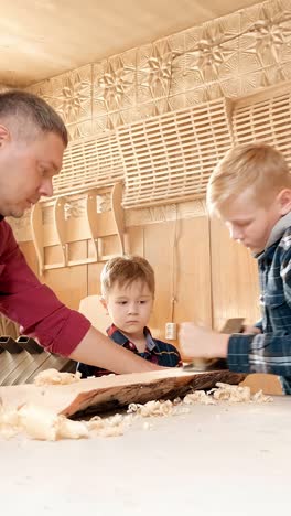 adult male woodworker guides two boys in woodworking activity, demonstrating craftsmanship and skill while creating wooden project in a workshop environment