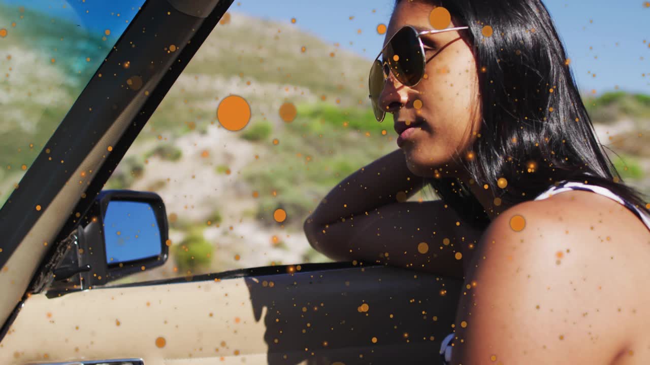 Automotive convertible moving along coast, particles drifting while passenger adjusting sunglasses