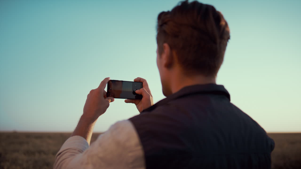 Farmer taking field picture with smartphone golden autumn sunlight rear view.