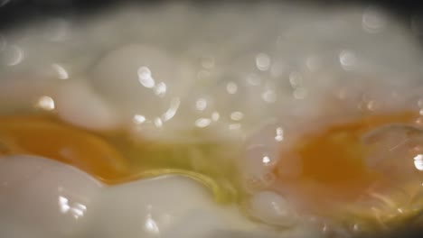 slide footage with soft bokeh close up of frying eggs in a black iron pan