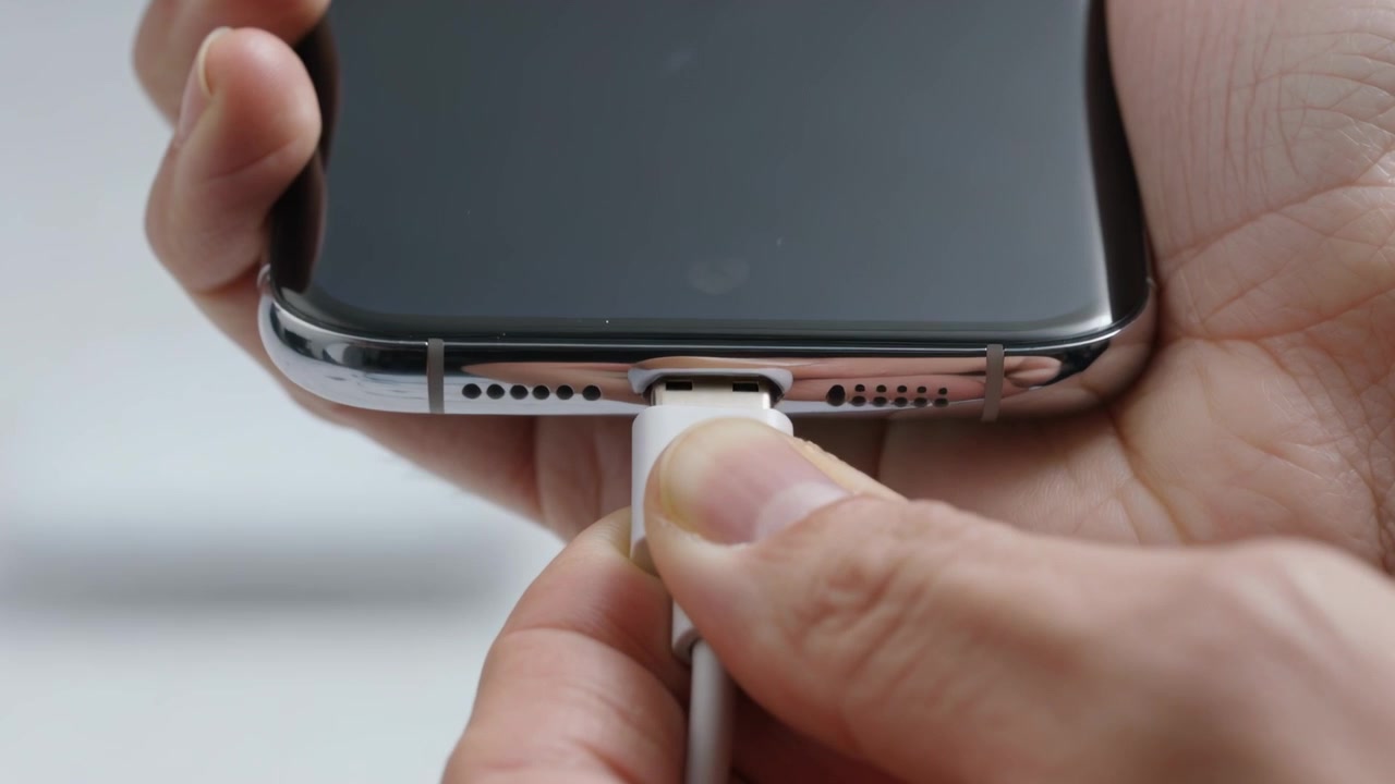 Posizionamento del cavo, mani che allineano e inseriscono nella porta inferiore del telefono in studio, caricando il telefono.