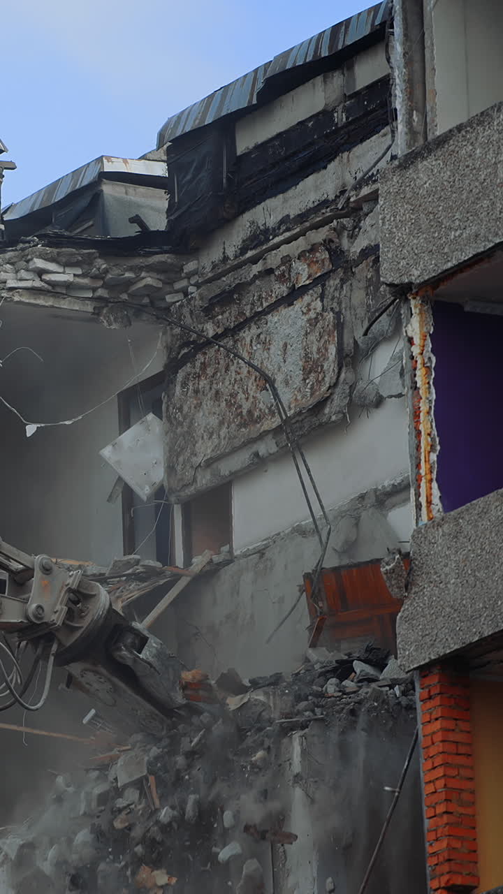 Powerful excavator claw dump the debris on the ground. Deconstruction site covering with the dust. Clear blue sky at the backdrop. Vertical video