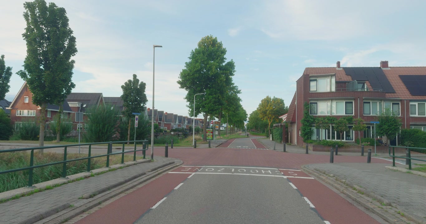 Veikryss i boliggate i Nederland med moderne murhus, solcellepaneler, sykkelsti og grønn skog under klar himmel med skyer