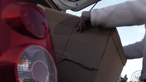 Woman-putting-cardboard-box-into-car-low-medium-shot