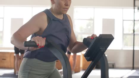 Determined-unaltered-caucasian-woman-training-on-elliptical-bike-at-gym,-in-slow-motion