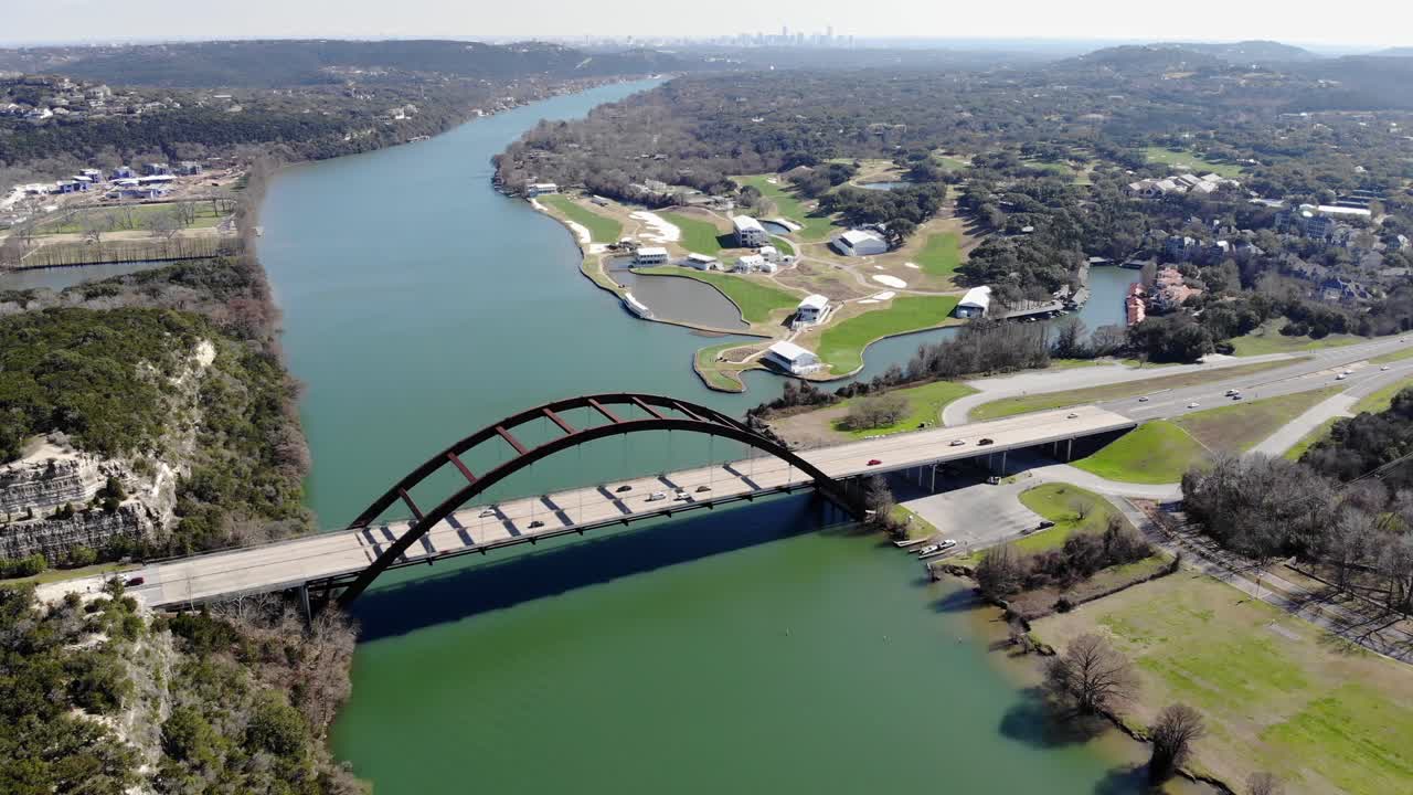 Aerial Austin Pennybacker Bridge - moving towards bridge set diagonally, higher altitude, skyline is far background with hazy sky