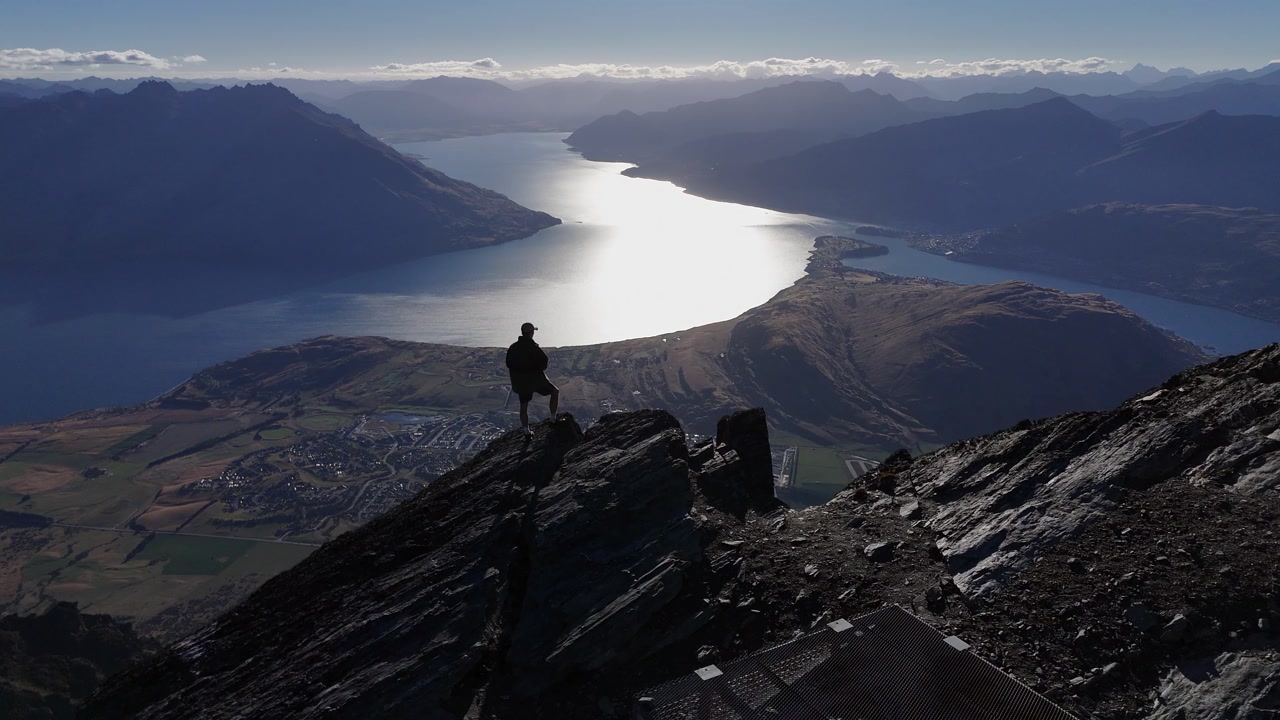 High contrast aerial silhouette: Man on summit above lake, Queenstown