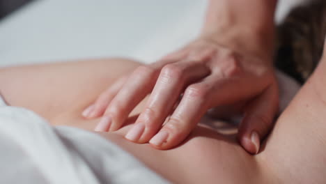 close up of therapist's hand performing soft massage strokes on exposed collarbone and shoulder of female client lying under white towel, emphasizing relaxation, and calming therapeutic touch