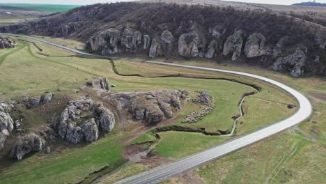 A-winding-road-through-dobrogea-gorges-surrounded-by-lush-greenery-and-rock-formations,-aerial-view