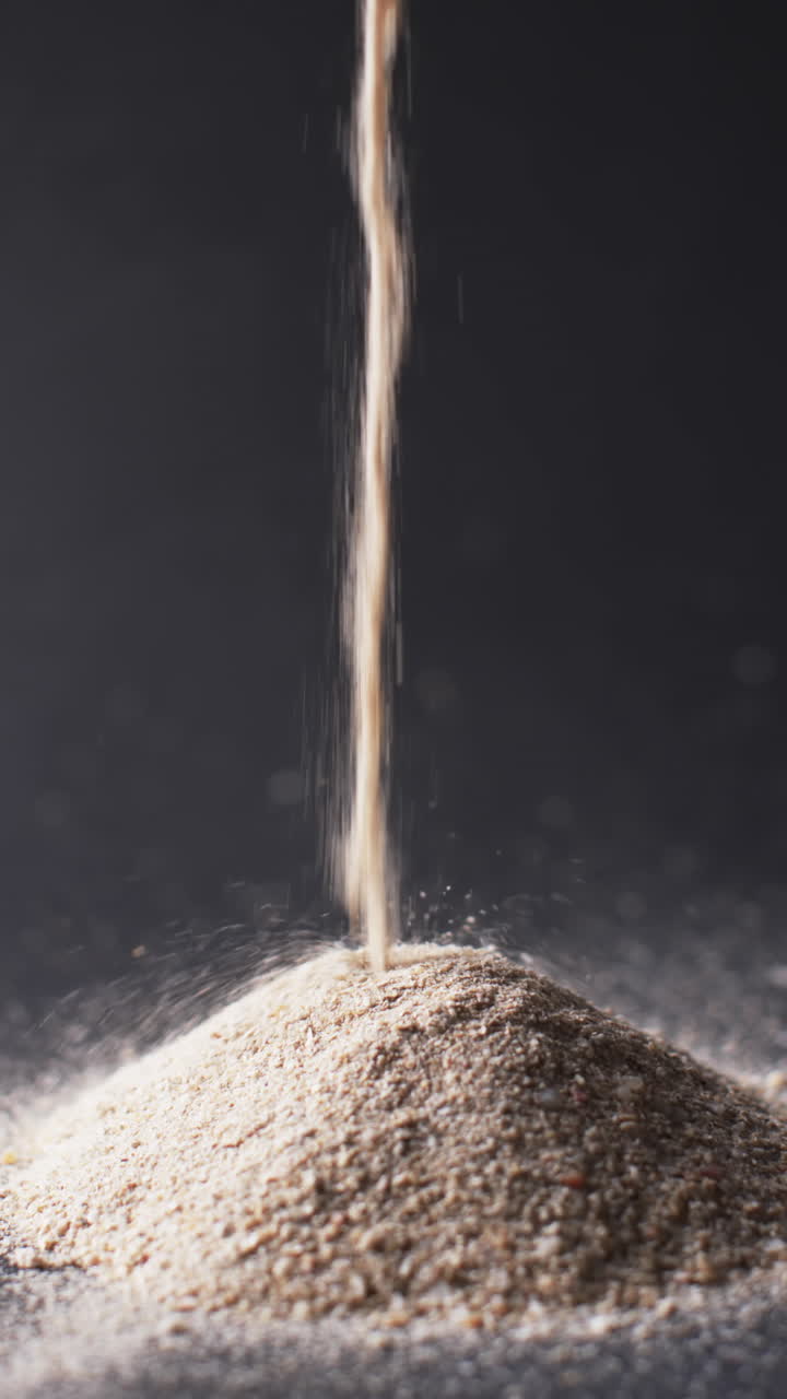 Vertical video of close up of heap of sand grains and copy space on black background