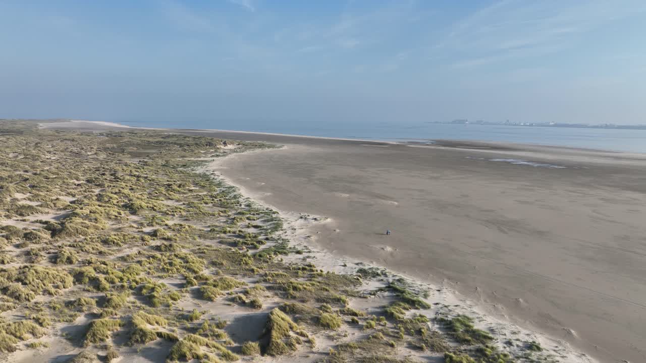 An aerial drone video of two people walking at the beach and in the dunes of Texel, Wadden island in The Netherlands.