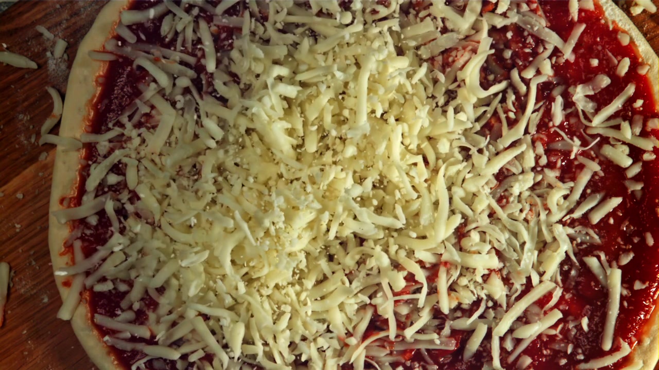 Cospargere mozzarella grattugiata su una pizza con salsa di pomodoro