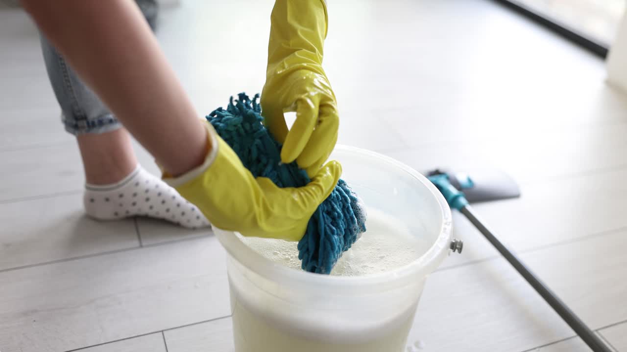 Person Wringing a Mop in a Bucket of Soapy Water