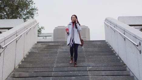 asian woman walking down the stairs talking on smartphone and holding takeaway coffee