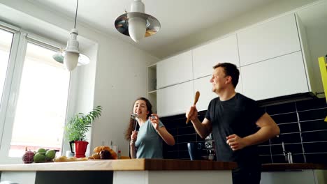 una pareja joven y alegre se divierten bailando y cantando mientras desayunan en la cocina de casa en vacaciones.