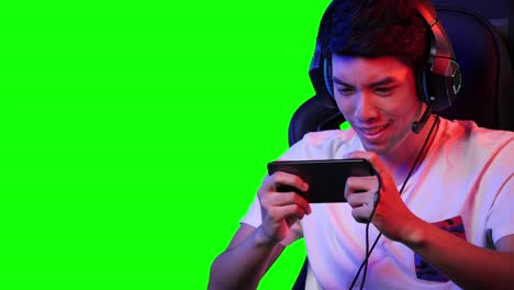 esports gamer hombre jugando juegos en línea en el teléfono inteligente en casa. hombre asiático controlando la consola con teléfono inteligente en el videojuego. joven juego de ocio en la sala de estudio y pantalla verde en casa.