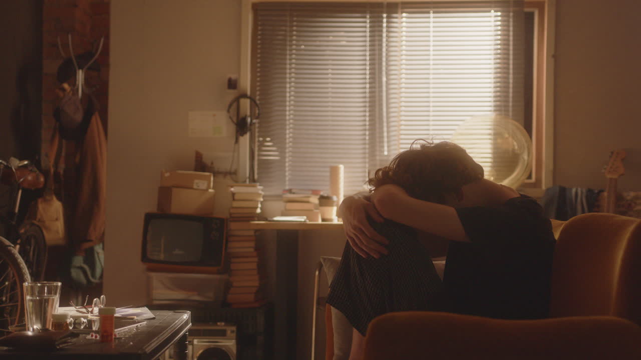 우울한 남자가 비는 방에 앉아 무을 둘러싼 팔로 구부러져 있습니다.