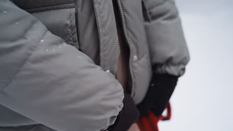 person wearing gray winter jacket and black gloves holding red dog leash in snowy environment, showing detail of hands and fabric textures, emphasizing outdoor pet walking, winter clothing, and cold weather