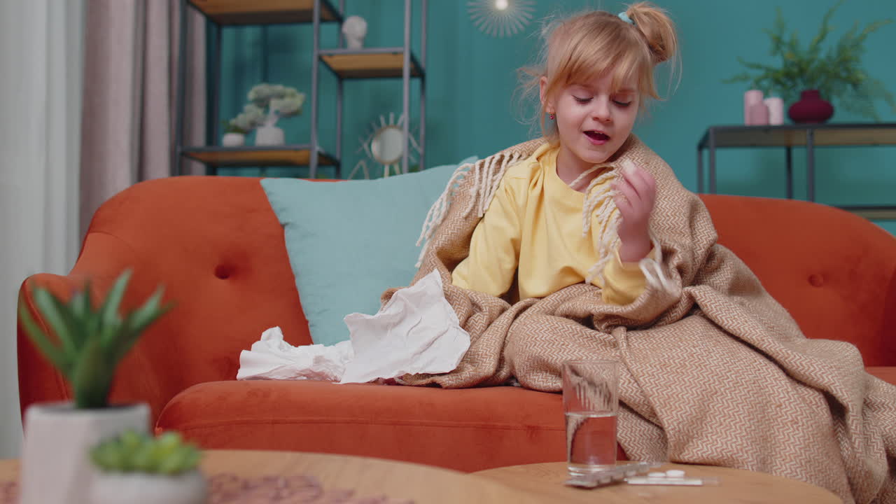 ребёнок с простудой страдает от лихорадки, аллергии, дует из носа, пьет лекарства, таблетки на диване дома.