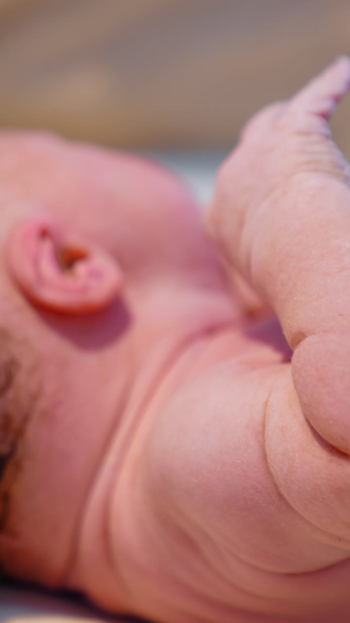 Mano con guanto in lattice blu accarezza la testa di un neonato. Un bambino caucasico giace sul tavolo. Primo piano. Video verticale.