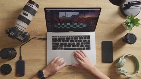 top view close up of male editor's hands using a laptop next to the camera editing the video in the workspace at home