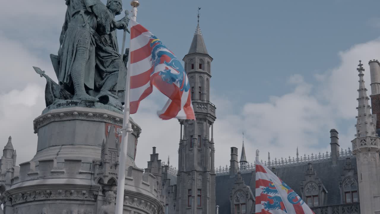 This image captures the essence of the Markt (Market Square) in Bruges, Belgium, dominated by the central Statue of Jan Breydel and Pieter de Coninck and the iconic Flag of Bruges