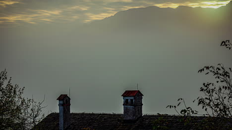 Low-clouds-and-high-cirrocumulus-clouds-at-sunset-above-a-roof-chimney---time-lapse