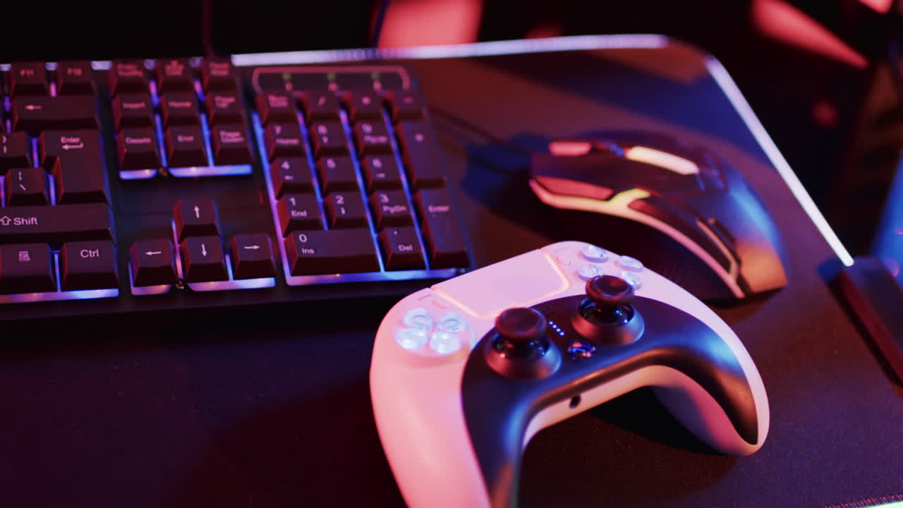 Video of computer keyboard and gaming equipment on desk with copy space on neon background