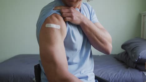 Midsection-of-caucasian-disabled-man-in-wheelchair-showing-bandage-on-arm-after-covid-vaccination