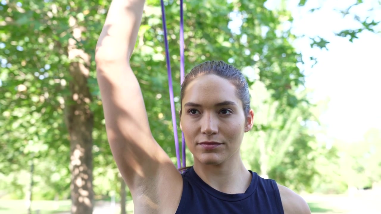 Una joven usa una banda de resistencia para hacer ejercicio al aire libre y mantenerse en forma en el parque.
