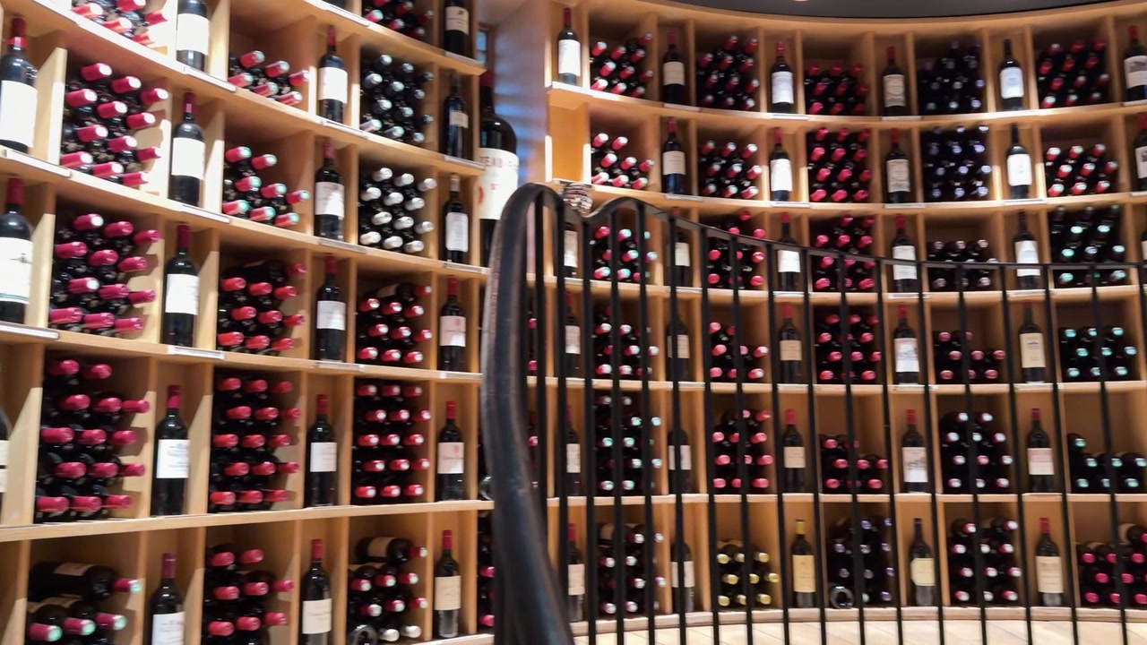 Una lenta panoramica rivela file di bottiglie di vino rosso su scaffali curvi in legno di una cantina.