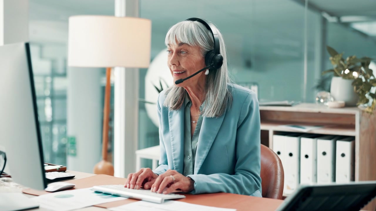 Senior Businesswoman Wearing Headset Working on Computer in Office