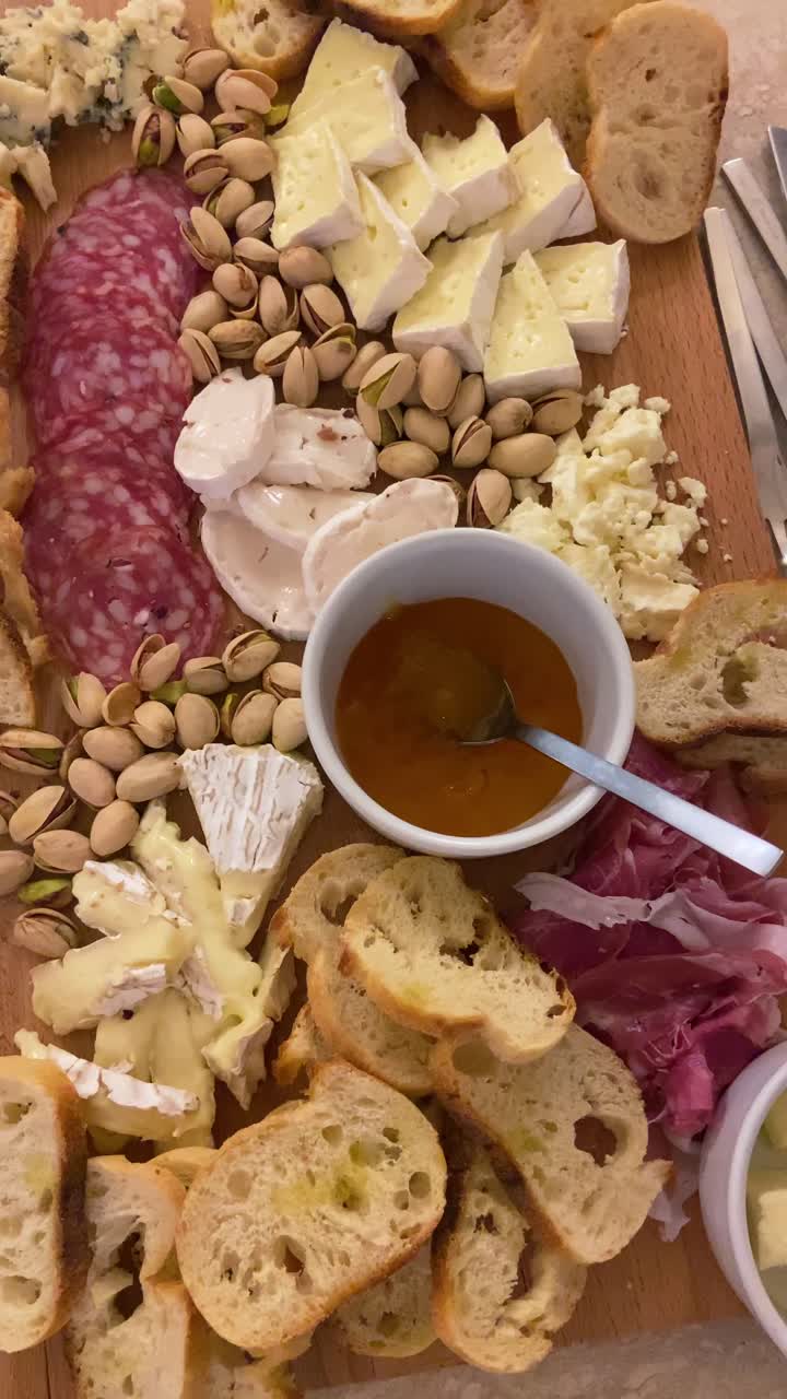 POV of wooden cheese and meat board charcuterie with cured meats pistachios fresh bread gourmet cheeses and apricot jam. Delicious and tasty snack appetizer for friends party. UGC style vertical reel