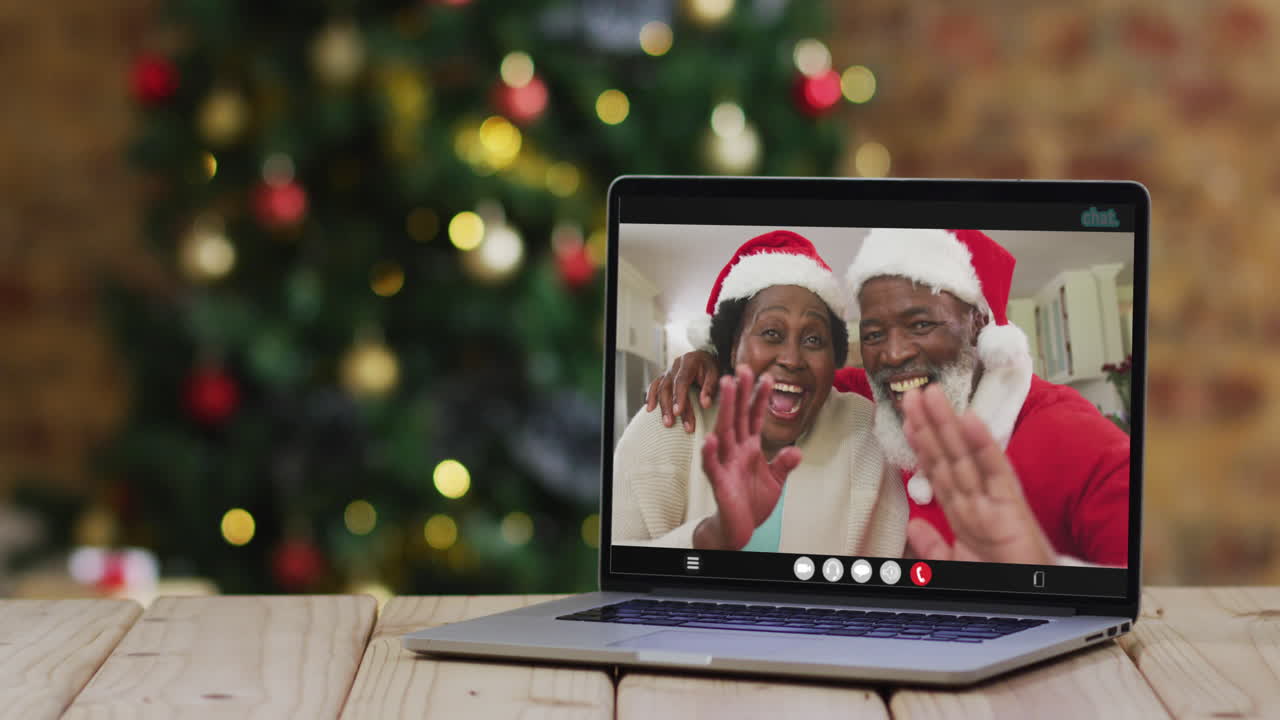 una pareja de ancianos afroamericanos con sombreros de santa en una videollamada en una computadora portátil, con un árbol de navidad