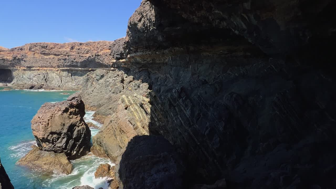 View from a dark, shadowy sea cave in Ajuy, looking at sunlit rock formations and turquoise ocean water. Fuerteventura, Canary Islands, Spain