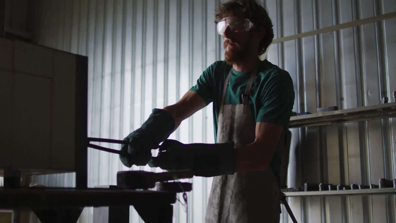 Caucasian male blacksmith holding hot metal tool in kiln with tongs in workshop
