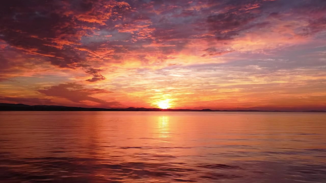 Ein atemberaubender Sonnenuntergang über ruhigem Wasser: Leuchtende Orange-, Pink- und Lilatöne spiegeln sich in den sanften Wellen wider und schaffen eine magische Szene der Naturschönheit.