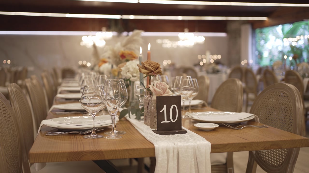 Long wooden banquet table set for wedding with glassware flowers candles and number sign
