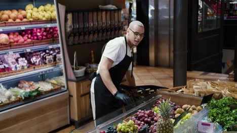 man worker in black apron and gloves stocking the fruits in supermarket