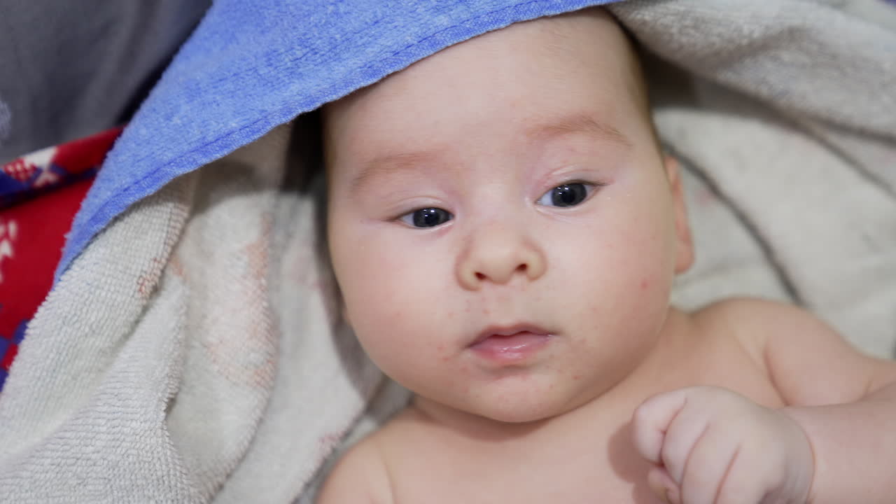 Cute child wrapped into a towel looking surprised into camera. Little kid relaxing after a bath. Close up.