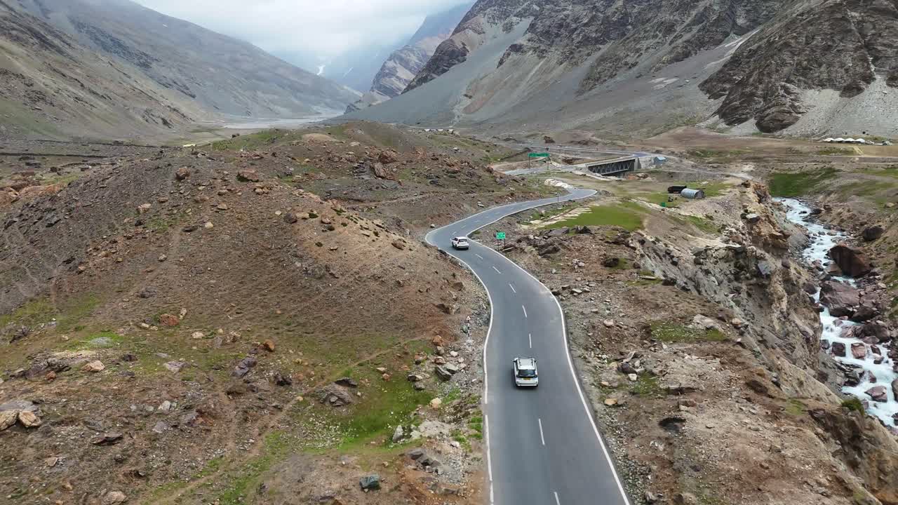 Aerial drone shot highlighting the twists and turns of a mountain highway with moving vehicles.