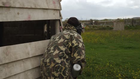 A-shor-following-a-person-in-a-painball-field,-revealing-more-team-members-hidden-behind-shelters