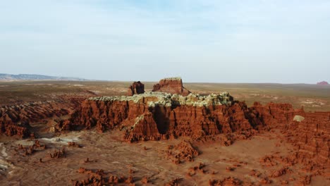 Gorgeous-dolly-in-aerial-drone-shot-of-the-beautiful-Goblin-Valley-Utah-State-Park-with-small-strange-mushroom-rock-formations-below-and-large-red-and-white-Butte's-in-the-background