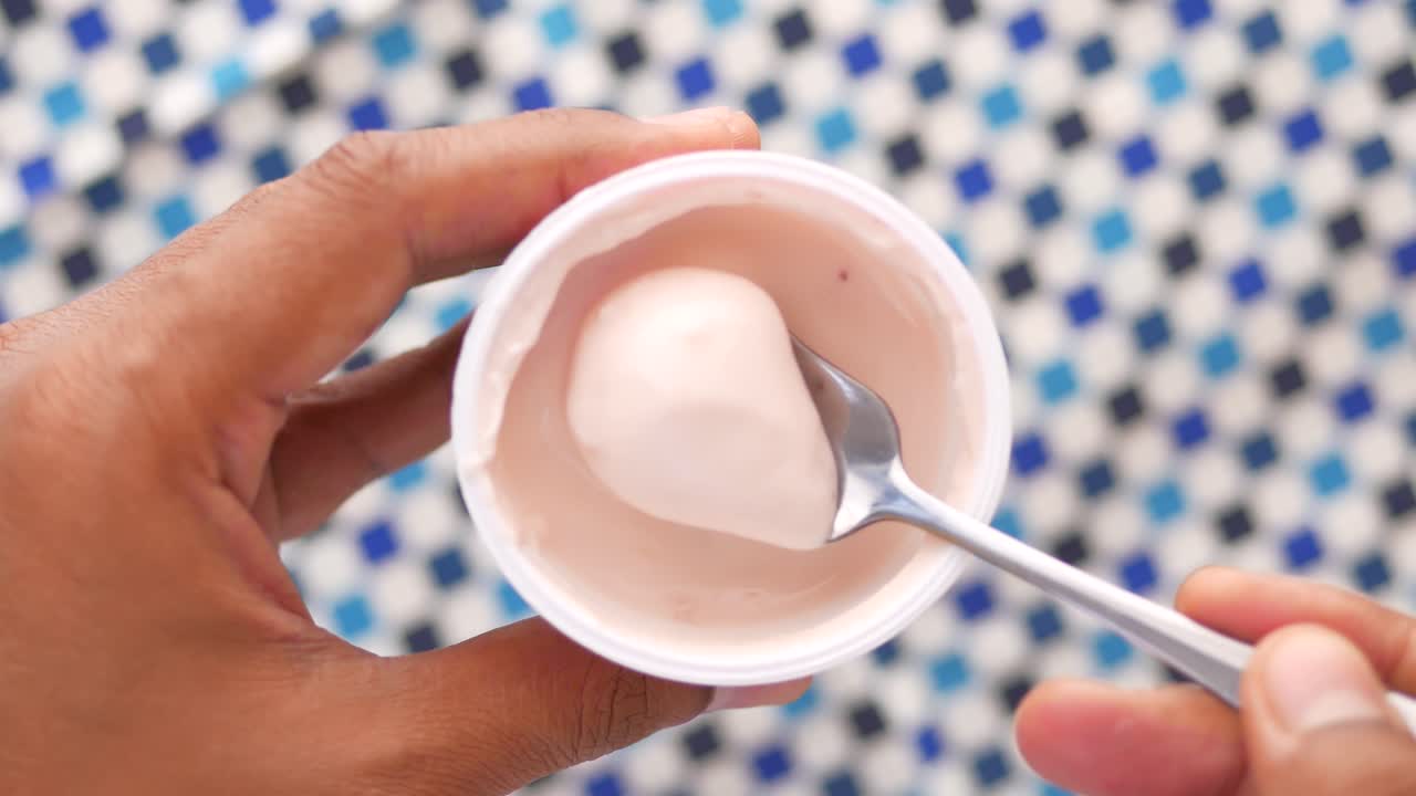 Iogurte fresco em um recipiente de plástico e colher na mesa