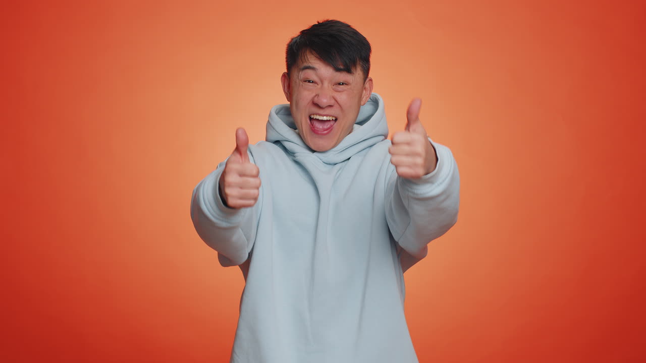Asian adult man raises thumbs up agrees or gives positive reply recommends advertisement likes good
