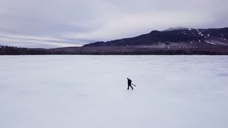 a man carries an ice auger across frozen fitzgerald pond, maine